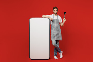 Full body young housekeeper chef cook baker man wear grey apron big huge blank screen mobile cell...