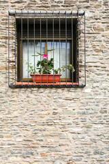Fototapeta na wymiar A light-coloured stone house with a barred window with a flower pot resting in it. Image has copy space.
