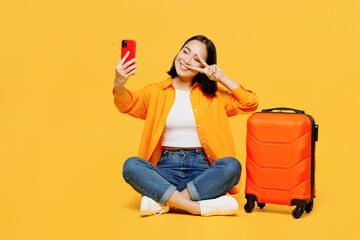 Young woman wears summer clothes sit suitcase do selfie shot on mobile cell phone isolated on plain...