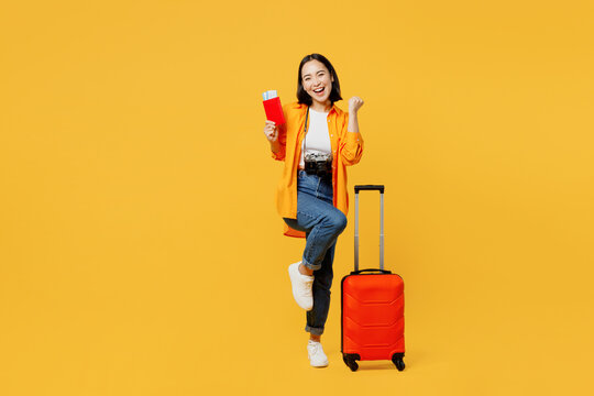 Young woman wears summer clothes hold passport ticket suitcase do winner gesture isolated on plain yellow background. Tourist travel abroad in free time rest getaway. Air flight trip journey concept.
