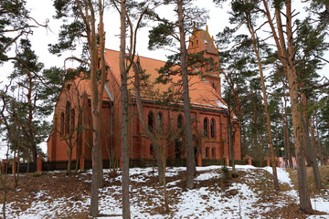 catholic church on a hill with melted snow in spring among pine trees