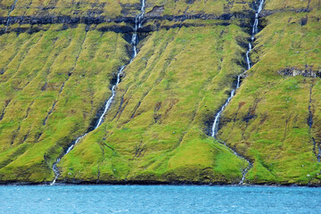 Rocky shore overgrown with grass with a waterfall