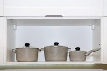 three pans in niche of kitchen cabinet. Utensils for cooking. White MDF kitchen cabinet with shelf