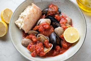 Beige plate with steamed mussels and littleneck clams in thick tomato broth, middle closeup, horizontal shot, selective focus
