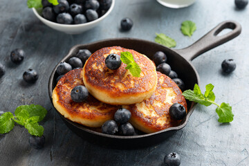 Cottage cheese pancakes served in cast iron frying pan with blueberries and mint leaves. Healthy breakfast food.