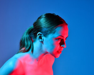 Head and shoulders close up portrait of pretty girl with expressive facial expressions, with  colourful neon gel lighting, isolated on studio background.