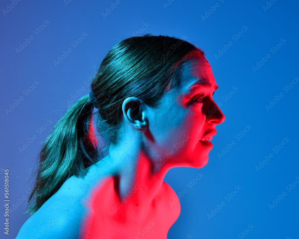 Poster Head and shoulders close up portrait of pretty girl with expressive facial expressions, with  colourful neon gel lighting, isolated on studio background.