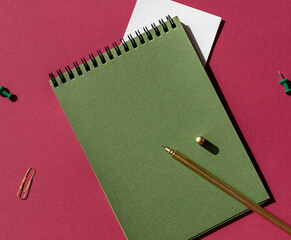 Green spiral notebook with white note paper, pen on the purple magenta color background. Copy space
