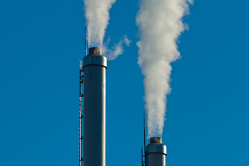 factory chimneys and white smoke against a blue sky