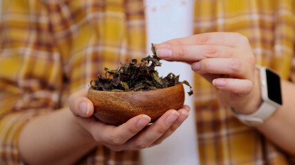 unrecognizable woman in a plaid shirt holds a wooden bowl and dried seaweed in her hands