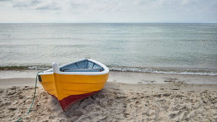 A small yellow fishing boat on the shore of a beach on the Baltic Sea in Poland - Powered by Adobe