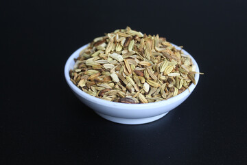 Dried granules of Aniseed, or Pimpinella Anisum seed, or Adas Manis, inside a bowl. Isolated on black background