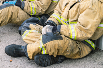 Firefighters in special protective clothing rest while sitting on the road. Firefighters' clothing...