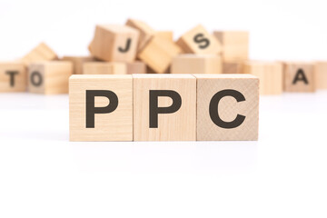 text PPC - Pay Per Click - is written on three wooden cubes standing on a white table. in the background - a mountain of wooden cubes with letters.