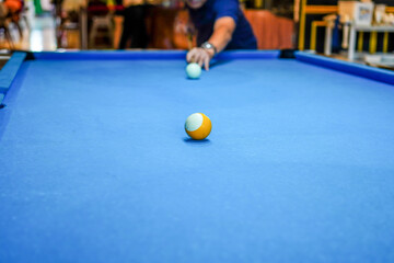 Players aim at the yellow billiard ball in the middle of the pool table. Blurred people in the background