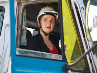 Engineer woman wears safety helmet sitting in a truck. Portrait of young female truck driver working at logistic shipping warehouse loading heavy merchandise cargo. Foreman and transportation service.