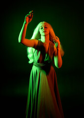 Fototapeta premium portrait of pretty girl with blonde hair & elegant gown with expressive facial expressions & gestural arm poses. colourful neon gel lighting, isolated on black studio background.