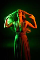 portrait of pretty girl with blonde hair & elegant gown with expressive facial expressions & gestural arm poses. colourful neon gel lighting, isolated on black studio background.