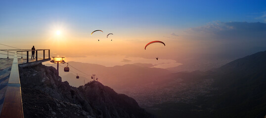 Leisure and skydiving from the Babadag mountain over the Fethiye resort, Turkey. Panoramic landscape with silhouettes of parasailing touristers flying near the top station of Oludeniz cable car. - 561530287