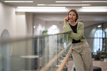 Successful self-sufficient woman talking on phone standing inside business center building calling...