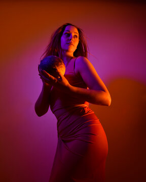 Low angle portrait of pretty girl wearing pink outfit, gestural arm poses reaching out as if casting a spell, colourful neon gel lighting, isolated on studio background.