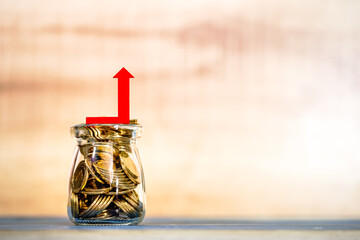 Bottle bank with gold coins inside and red arrow graph with growing value on the top put on the...