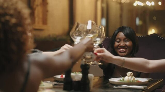 beautiful ladies celebrating meeting in restaurant, friends clinking glasses and drinking champagne