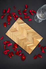 Wooden cutting board for cooking on a dark black background with a glass of wine and red rose petals. View from the top.