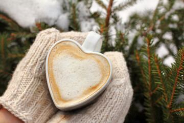 foamy cappuccino in a heart-shaped mug in hands dressed in mittens. warm drink on a winter day