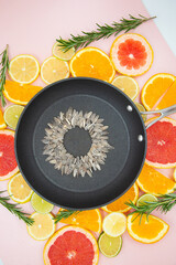 background of slices of citrus fruits, oranges, lemons, limes, grapefruits, on which a black pan is placed, inside which a sunflower flower is made from sunflower seeds. View from the top.