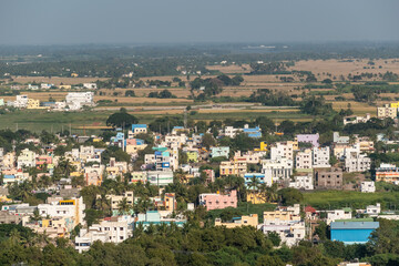 Aerial view of low rise buildings and houses surrounded by green farmland in the town of Trichy in Tamil Nadu, India.