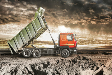 A dump truck unloads sand at a construction site. Machine for the transportation of bulk cargo with a raised body. Construction site at sunset. Equipment for earthworks.