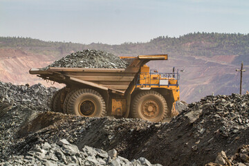 Obraz premium Large dump truck for removal of rock mass from the quarry for open-pit mining of minerals. Initial stage of melalurgy, machinery for the extraction of raw ore.