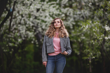 Obraz premium Confident woman in spring or summer nature against background of flowering trees. Model with long curly hair