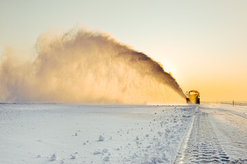 Bulldozer removes snow from the ice road at sunset.