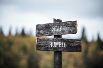 vintage and rustic wooden signpost with the weathered text quote stay humble, outdoors in nature. blurred out forest fall colors in the background.