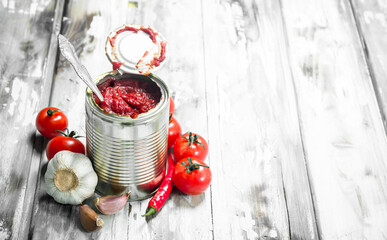 Tomato sauce in a tin can with a spoon and tomatoes.