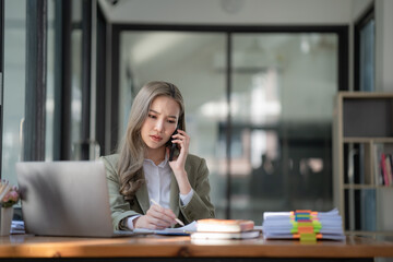 Stressed millennial Asian businesswoman or female manager having a serious phone call with her business client while working in the office. - obrazy, fototapety, plakaty