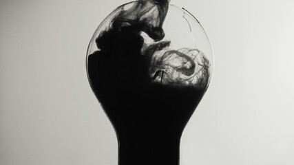 Black smoke. Broken light bulb. Ink water shot. Dark energy. Toxic fume cloud filling cracked glass lamp on white abstract copy space background.