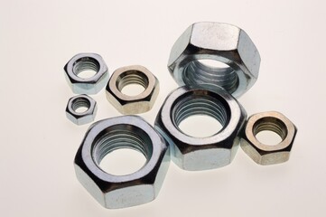 New, chrome-plated bolts and nuts of different sizes lie on a white background. Close-up