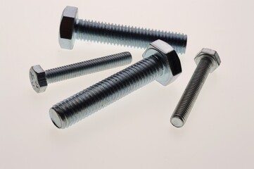 New, chrome-plated bolts and nuts of different sizes lie on a white background. Close-up