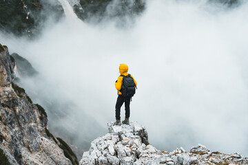 Obraz premium Back view of climber standing on rock on mountain summit and looking at view. Spectacular scenery with hiker above the clouds. Succes and achievement concept