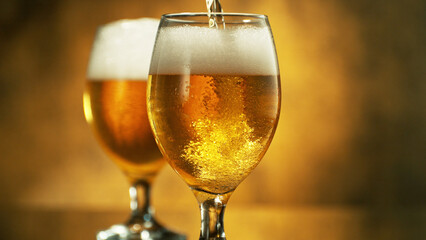 Glass of pouring light beer on dark golden background.