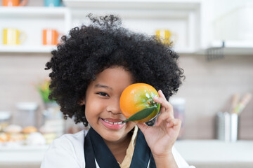 Happy African American child girl holding orange in the kitchen. Smiling child girl with fruit in the kitchen