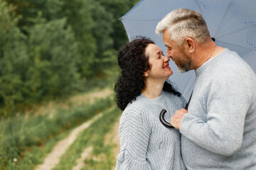 Fototapeta premium Senior couple standing in a park and looking on each other under umbrella