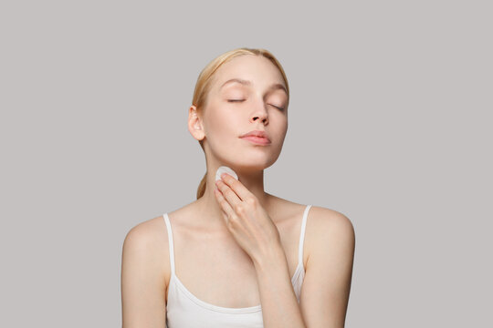 Beauty, skincare and facial treatment concept. Young woman cleaning her face with cotton disk on white