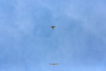 A single-engine aircraft is towing a glider. Bottom view.