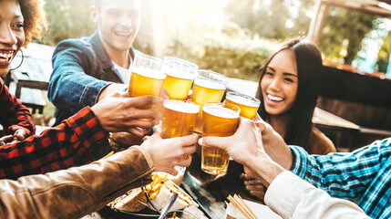 Happy multiracial friends cheering beer glasses at brewery pub garden - Group of young people...
