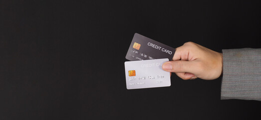 Hand is hold two credit cards. Black and silver color credit cards isolated on black background.