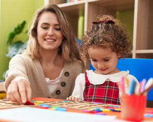 Fototapeta premium Teacher and toddler playing with maths puzzle game sitting on table at kindergarten